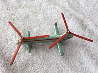 Top angled view showing light green helicopter body with red rotors and side windows, resting on white textured fabric.