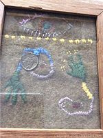 Frontal image of framed textile artwork under glass showing embroidered hands and geometric shapes.