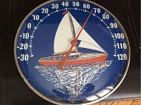 Front view of the round vintage thermometer showing sailboat on water design and temperature dial.