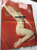 Color photo showing large nude Marilyn Monroe on red background poster with pencil for scale, folded with visible creases.
