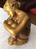 Front angled view of the gold-painted chalk-ware statue depicting a seated nude woman with hair in a bun showing the texture and paint finish.