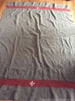 Full view of the gray wool military blanket with red bands and white Swiss crosses