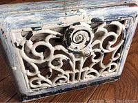 Close-up image of the front of a painted cast iron vent grate with visible peeling paint and ornate design