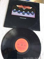 Photo showing black vinyl record with red and orange center label and its cover with Aerosmith logo and knobs image.