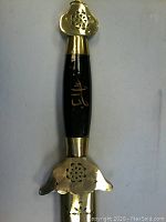 Close-up of the sword handle showing black and gold detailing with Chinese character and floral cutouts on guard and pommel.