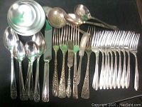 Top view of 32 silver plated pieces including forks, spoons, serving ladles, a butter spreader, and a knife, laid out on surface