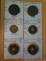 Photo of six Chinese coins mounted in white holders with handwritten notes showing dates ranging from 1023 to 1906 and some catalog references.