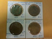 Four vintage brass brothel tokens housed in white cardboard holders with handwritten labels indicating their origin and details.