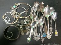 Overview of lot showing arranged jewelry and spoons on dark background