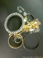 Top view of assorted silver and gold-tone costume jewelry with bracelets, rings, and necklaces on a dark surface