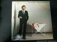 Front cover of the Eric Clapton Money and Cigarettes LP depicting Clapton in a suit near an ironing board with artistic design.