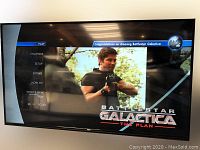 Front view of 65" RCA LED TV powered on, showing Battlestar Galactica menu and visible screen line