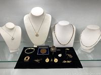 Full overview of five necklaces displayed on busts with assorted small jewellery in front on black velvet mat.