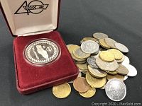 Overview photo showing a pile of various coins alongside a red velvet display case containing a commemorative medallion