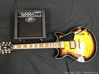 Full view of the sunburst Ibanez guitar laid next to the Peavey amp on a black background