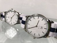 Two JWLS quartz watches on white and blue nylon straps, showing watch face and side angle.