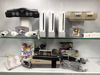 Overview of two glass shelves displaying six consoles, games and accessories