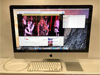 iMac powered on displaying YouTube video, front view with keyboard, trackpad, power cable.
