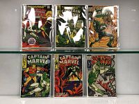 Six Captain Marvel comics in protective sleeves, arranged in two rows on a glass surface, showing cover art and overall condition.