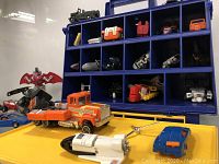 Display of various GoBots toys on a blue cubby organizer and yellow shelf showing multiple vehicles and figures.