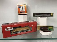 Four model trains and cars displayed with boxes, including Lionel locomotive, Atlas freight car, Minitrix passenger car, and JCT hopper car.
