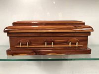Closed coffin-shaped wooden storage box with handle-like accents and polished wood finish.
