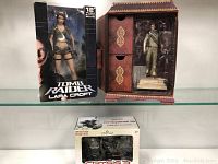 Three boxed video game collectible figures: Tomb Raider Lara Croft, Uncharted Nathan Drake, and Crysis 3 Prophet.