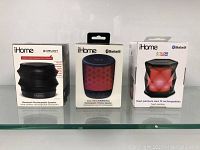 Front view of three new iHome Bluetooth speakers in their boxes showing brand and main features including color changing and voice control.