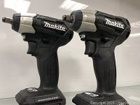 Front angled view of two Makita impact drivers side-by-side showing black and silver bodies with Makita branding.