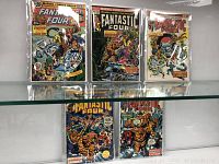 Five Fantastic Four comics displayed on shelf, seen through glass shelf edge.