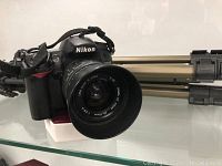 Front view of Nikon D7000 body with attached Sigma lens and tripod in background