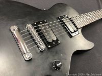 Close-up of pickups, bridge, and volume knob showing black humbucker pickups and chrome hardware on black guitar body.