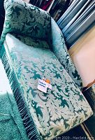 Side view of the fabric chaise lounge featuring green and light blue/gray damask fabric and tassel fringe trim.