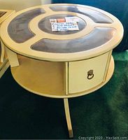 View showing round coffee table with curved legs, cream and brown colors, central note describing contents.