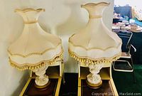 Wide angle view of both vintage formal lamps showing the full height and width including the detailed fabric shades with tassels and carved bases.