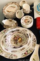 Full view of the china set including stacked dinner plates, cups with saucers, large bowls, and gravy set arranged on a table.