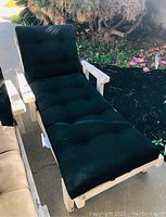 Front view of one white wooden lounge chair with black cushions showing seat and backrest padded cushions outside on concrete surface.