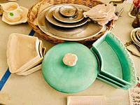 Photo showing woven pecan bag, stacked metal lazy Susan trays, cream and green ceramic trays, and candle holder.