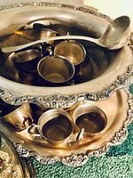 Silver punch bowl filled with cups and ladle, floral embossed rim visible