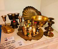 Gold plated set of assorted kitchen and tableware items displayed on a table, including trays, salt and pepper shakers, bowls, goblets, and candle holders.