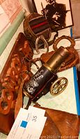 Photo showing wooden carved plaque spelling 'CANYON', miniature canteen styled as a vintage cannon, round woven bag, leather bags, framed cowboy photo in background.