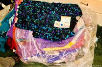Pile of assorted women's clothing including dresses, suits and blouses with top item a teal and purple sequined dress