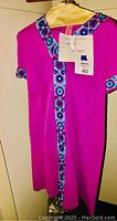 Bright pink vintage dress with blue, white, and purple floral trim hanging on hanger