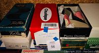Photo of stacked shoeboxes with several women's shoe brands visible, including Colloque and Pierre Dumas. Eight pairs of shoes total.