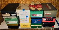 Stack of 13 women's shoe boxes with some brand visibility and one pair of red rhinestone sandals on top
