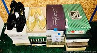 Wide shot of 14 pairs of women's shoes on top of and beside shoeboxes, including black patent leather strappy heels and light gold flats.
