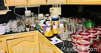 Wide shot of counter with numerous glass sets, mugs and glasses arranged in groups including red rimmed glasses and colorful mugs