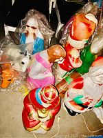 Vintage Christmas lawn decorations including multiple Santa figures, Wise Men, a nativity person, and a painted horse figure, some figures still in plastic wrap, all shown on a floor surface.