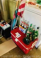 Photo showing red Igloo cooler with Pepsi logo, glass soda bottles on top, and folded U.S. flag on pole beside it.