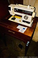 Full view of the white vintage sewing machine mounted on the wooden cabinet with drawer and pedal.
